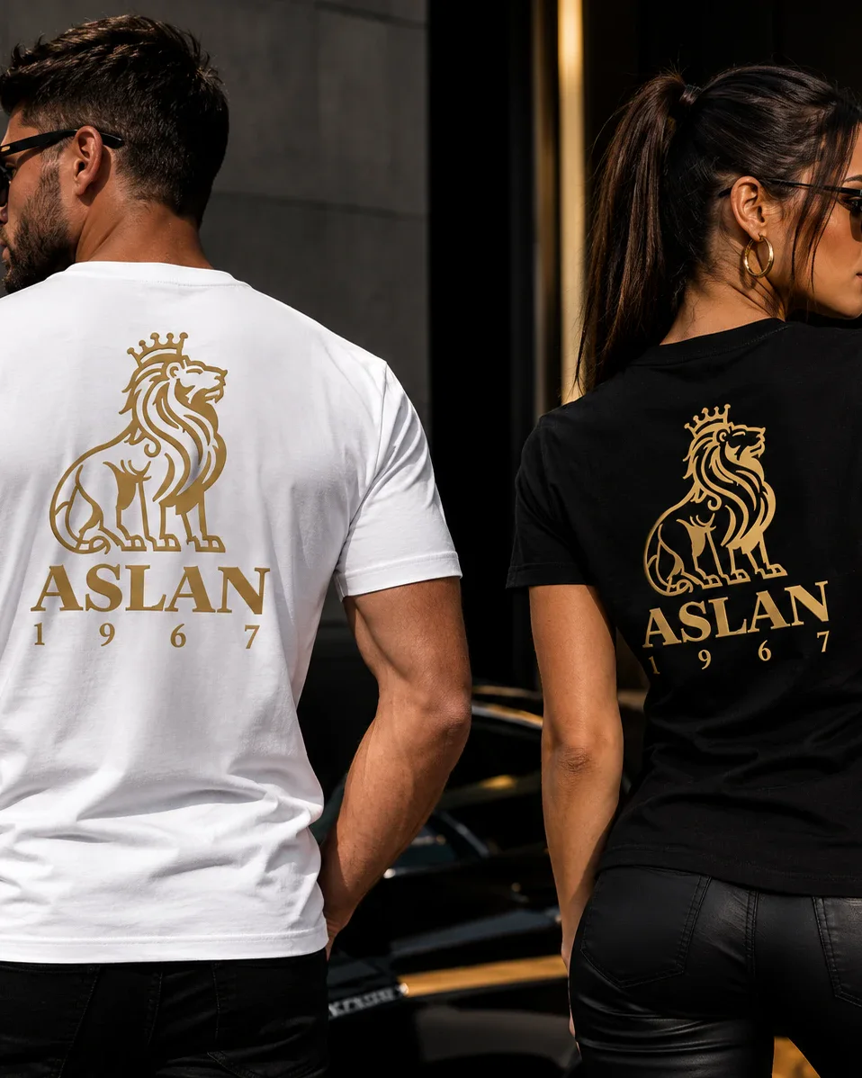 Un homme en T-shirt blanc et une femme en T-shirt noir ASLAN 1967, vus de dos, grand lion doré imprimé.